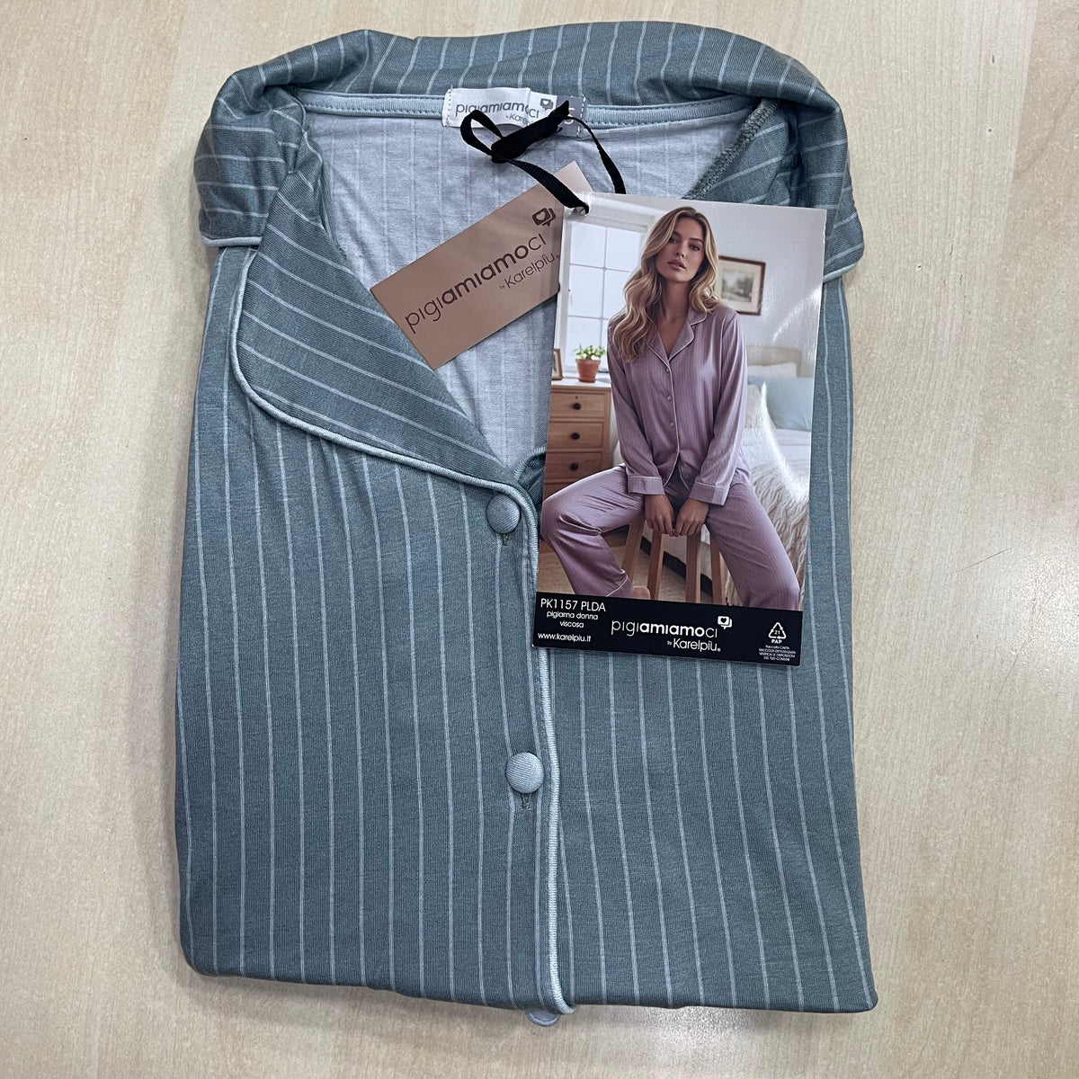 Pigiama da donna Pigiamiamoci colore azzurro fiume piegato su piano in legno con colletto aperto, bottoni foderati e cartellino