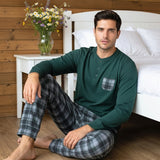 Modello che indossa il pigiama da uomo Karelpiù 1234 in caldo cotone verde con maglia serafino a 3 bottoni e pantalone a quadri seduto accanto al letto