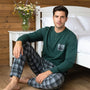 Modello che indossa il pigiama da uomo Karelpiù 1234 in caldo cotone verde con maglia serafino a 3 bottoni e pantalone a quadri seduto accanto al letto