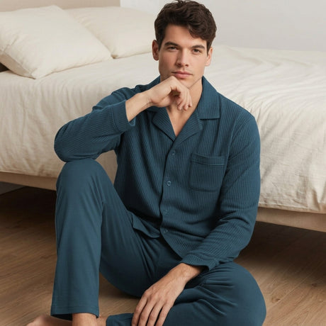 Modello uomo seduto accanto al letto che indossa il completo pigiama in caldo cotone color laguna Pigiamiamoci 1445 aperto con bottoni
